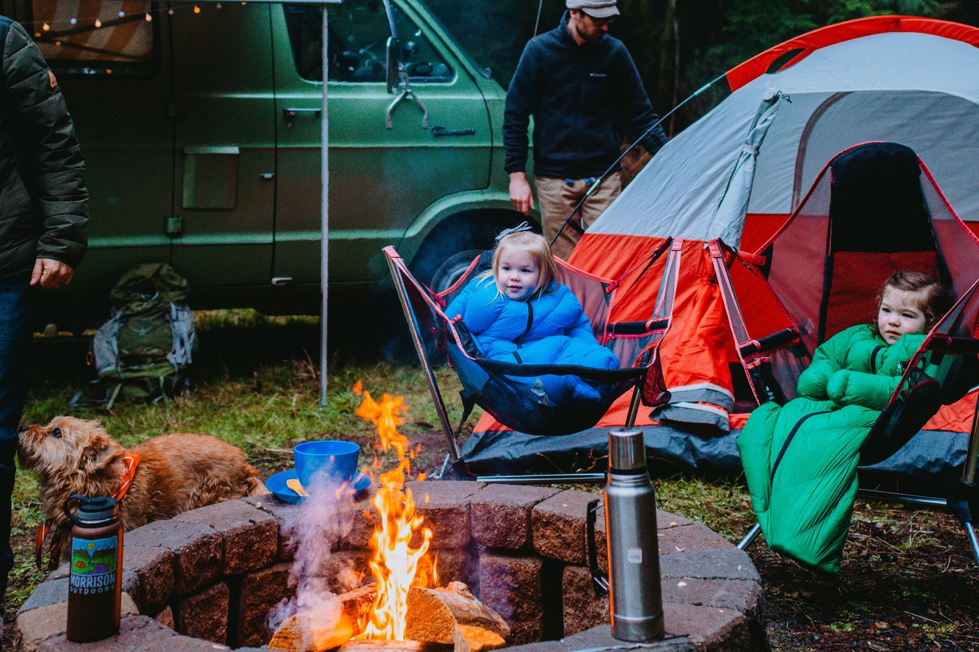 Baby and Toddler in Big Mo and Little Mo sleeping bags camping sitting around a campfire warm and happy and smiling.