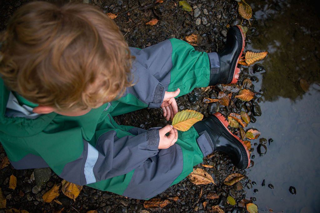 Child playing with leaves by a puddle on a leafy ground